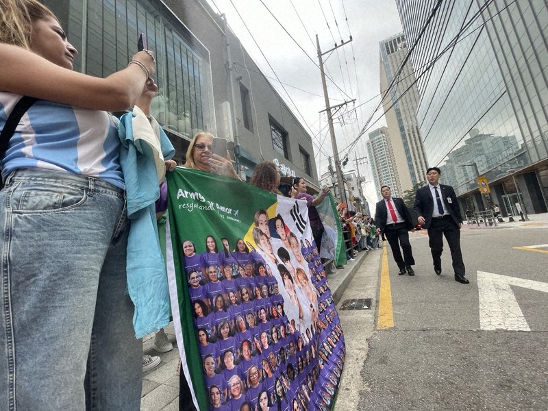 BTSのRMさんとVさんの除隊を祝い、所属するHYBE本社前に集まったファンら。警備員が車道を確保しようと巡回していた＝ソウル市内で2025年6月10日午前、堀山明子撮影