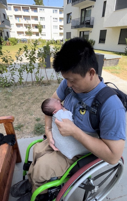 自宅アパートの中庭で、生後1週間ほどの娘を腹巻きに入れる諏訪正晃さん＝ベルリンで2024年9月7日、五十嵐朋子撮影