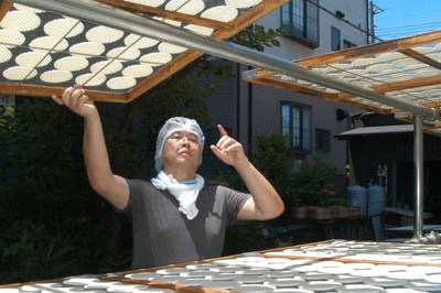 干し網に並べたせんべいの生地を天日干しする岩立規史さん＝埼玉県草加市で2025年6月22日午前10時59分、山下貴史撮影