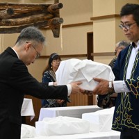 吉田英一郎・国土交通審議官（左）からアイヌ民族の遺骨を受け取る、小樽市のアイヌ関連団体「インカルシペの会」の安ケ平拓也さん＝白老町で2025年7月14日午前11時9分、森原彩子撮影