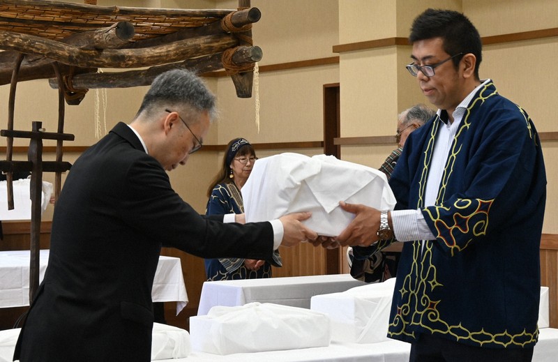吉田英一郎・国土交通審議官（左）からアイヌ民族の遺骨を受け取る、小樽市のアイヌ関連団体「インカルシペの会」の安ケ平拓也さん＝白老町で2025年7月14日午前11時9分、森原彩子撮影