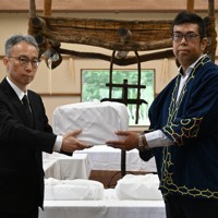 吉田英一郎・国土交通審議官（左）からアイヌ民族の遺骨を受け取る、小樽市のアイヌ関連団体「インカルシペの会」の安ケ平拓也さん＝白老町で2025年7月14日午前11時7分、森原彩子撮影