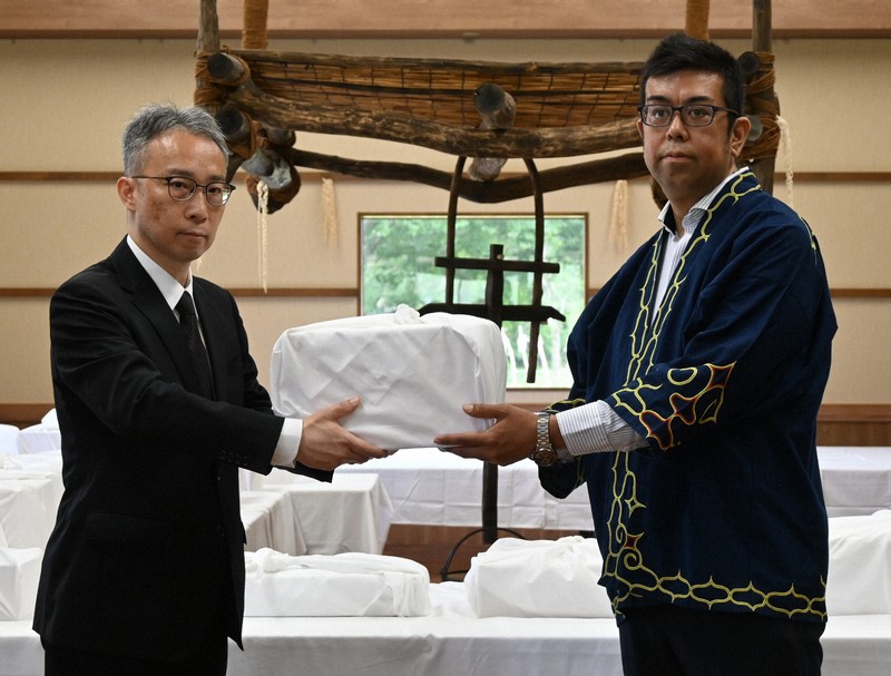 吉田英一郎・国土交通審議官（左）からアイヌ民族の遺骨を受け取る、小樽市のアイヌ関連団体「インカルシペの会」の安ケ平拓也さん＝白老町で2025年7月14日午前11時7分、森原彩子撮影