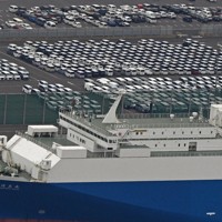 日産自動車九州苅田工場に隣接する港湾エリアに並ぶ完成した乗用車。手前は輸出車の運搬船＝福岡県苅田町で2025年4月10日午前10時46分、本社ヘリから上入来尚撮影