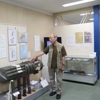 太平洋戦争で米軍が日本に投下した焼夷（しょうい）弾の模型を解説する、吉田裕・一橋大名誉教授。東京大空襲・戦災資料センターの館長を務めている＝東京都江東区の同センターで2025年8月6日、栗原俊雄撮影