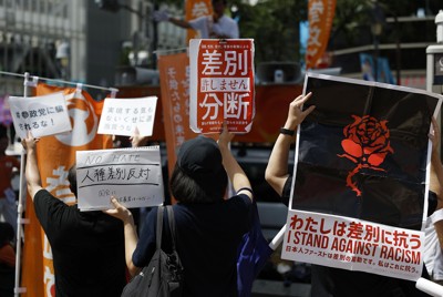 参政党候補者の街頭演説に抗議のメッセージを掲げる人たち（東京・渋谷で7月19日、共同通信）