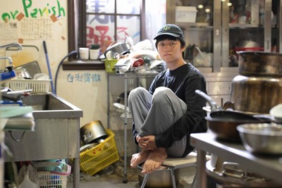 京大吉田寮食堂の調理場に座る寮生の奥山朱凜（しゅり）さん（21）。「寮は経済的に困窮する学生が勉強を続けるためのセーフティーネット。和解を対話再開の契機として、大学は寮生と向き合ってほしい」＝京都市左京区で2025年10月2日、山崎一輝撮影