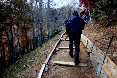 次男、健さんのために「いつまでもいっしょだよ」と書かれた銘標を持って上がる美谷島善昭さん＝群馬県上野村で2025年11月14日午後1時8分、喜屋武真之介撮影