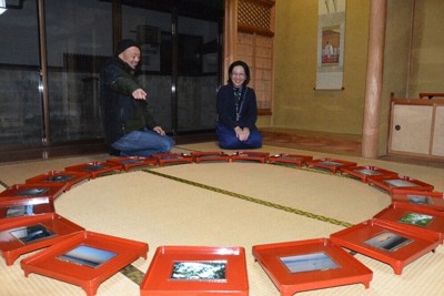 巫女の掛け軸（右奥）と朱塗り膳に乗せた写真について説明する高嶋敏展さん（左）＝松江市殿町のギャラリー殿町プラスで、村瀬達男撮影