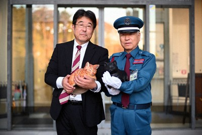 尾道市立美術館の正面入り口前で、黒猫のケンちゃんの置物を抱く警備員の馬屋原定雄さん（右）とゴッちゃんの置物を抱く梅林信二さん＝尾道市で、佐藤賢二郎撮影