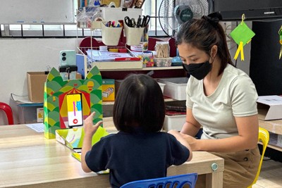 幼稚園の教室でブロックを積むよう促され、スマートフォンの画面を見ながら手を動かす女児＝マレーシア・サラワク州で（トイエイト提供）