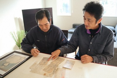 新さんが出征中に家族に宛てた手紙を見る（左から）長男粲さんと孫の新五さん親子。卓上にあるのは新さんの遺影＝福岡県筑後市馬間田で2025年12月15日午後2時20分、谷由美子撮影