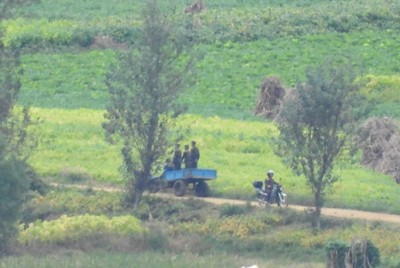北朝鮮の農村地帯で、バイクに乗る男性（右）。左側にはトラックの荷台に乗る兵士たち＝韓国北西部・金浦市から2025年10月9日午後2時21分、福岡静哉撮影（超望遠カメラを使用）