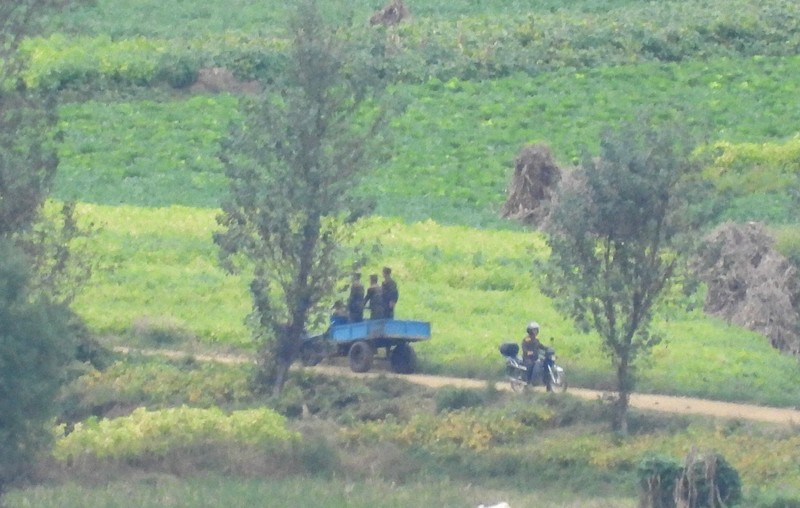 北朝鮮の農村地帯で、バイクに乗る男性（右）。左側にはトラックの荷台に乗る兵士たち＝韓国北西部・金浦市から2025年10月9日午後2時21分、福岡静哉撮影（超望遠カメラを使用）