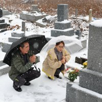 地震で母と兄を亡くし、元旦の命日に墓前で手を合わせる舩本悦司さん（70）と妻淳子さん（68）。悦司さんは「母は元気だったから。地震さえなければもっと長生きできたのにと思わずにはいられない。向こうで皆仲良く過ごして欲しい」と悼んだ＝石川県珠洲市で2026年1月1日午前9時23分、滝川大貴撮影
