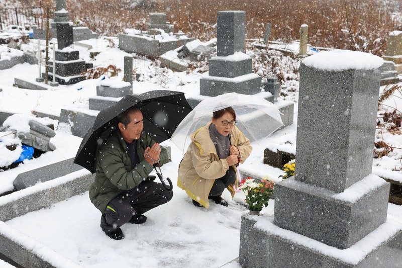 地震で母と兄を亡くし、元旦の命日に墓前で手を合わせる舩本悦司さん（70）と妻淳子さん（68）。悦司さんは「母は元気だったから。地震さえなければもっと長生きできたのにと思わずにはいられない。向こうで皆仲良く過ごして欲しい」と悼んだ＝石川県珠洲市で2026年1月1日午前9時23分、滝川大貴撮影