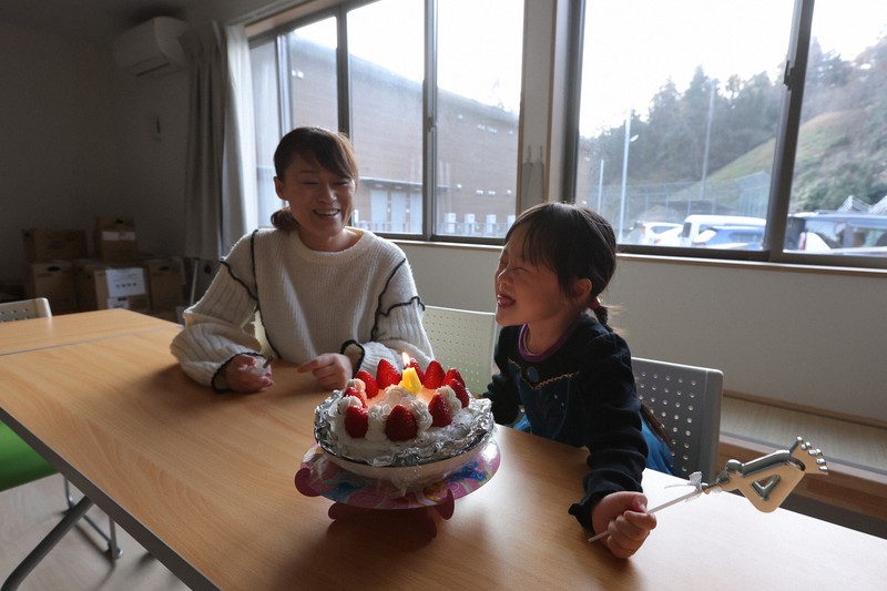 仮設住宅の集会所で長女・仁那ちゃん（右）の4歳の誕生日を祝うシングルマザーの脇田友里恵さん。お店で売っていたケーキは高価だったため手作りし、仮設住宅の敷地で遊べるようにスノーブーツとキックスケーターをプレゼントした＝石川県珠洲市で2025年12月28日、中川祐一撮影