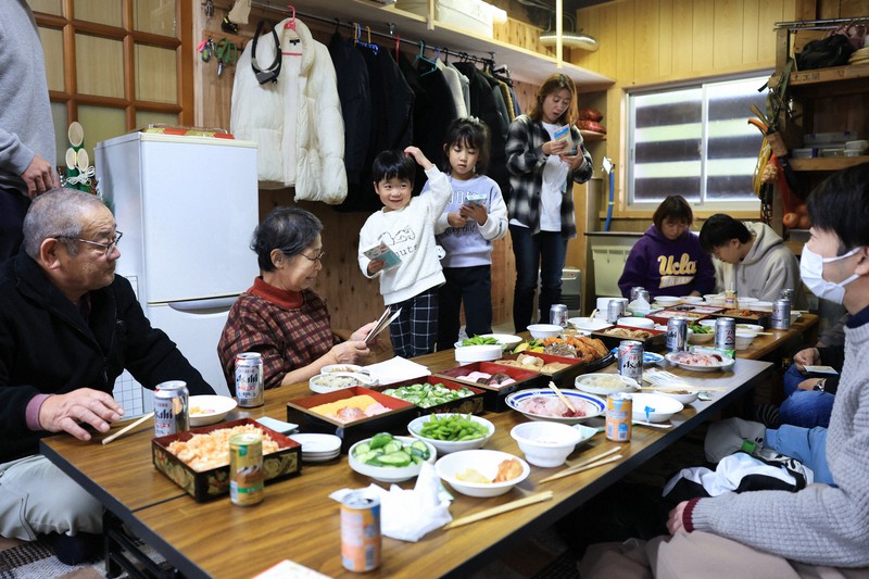 輪島市の渋洞福子さん一家は元旦、2年ぶりに親族が集まった。家は土砂ダムの影響で水没。現在は離れを改装して住んでいて、玄関にマットを引いて親族が座る場所を確保した。「2年前の続きができたみたい。みんな元気で1年を過ごしたい」＝石川県輪島市で2026年1月1日午後0時36分、滝川大貴撮影