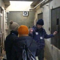 ツキノワグマの獣舎の前で「冬眠ツアー」の参加者に解説する飼育担当者（右）＝盛岡市動物公園で2026年1月10日（同園提供）