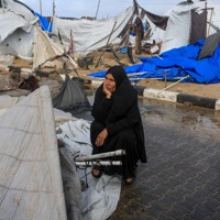 暴風雨の中、壊れたテントの近くに座りこむ女性＝パレスチナ自治区ガザ地区北部ガザ市で2026年1月13日、ロイター