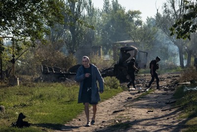 ドローンによる攻撃を受けた住宅街を歩く住民。後方は現場を調べる警察官と焼けたトラック。周辺では八つの民家と多くの車が破壊された＝ドネツク州スラビャンスクで2025年8月20日、写真家の尾崎孝史さん撮影
