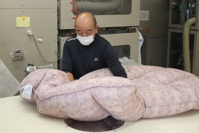 羽毛が入った機械のホースを生地に差し込むと、ふかふかの布団ができあがった＝山梨県富士吉田市富士見4で2025年10月23日午後3時33分、野田樹撮影
