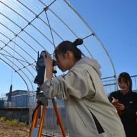 鉄の重りをぶら下げたビニールハウスの特定の点までの距離などを測量機器で測り、値をメモする福井工業高専の学生たち＝福井県鯖江市で2025年12月18日午前11時25分、萱原健一撮影