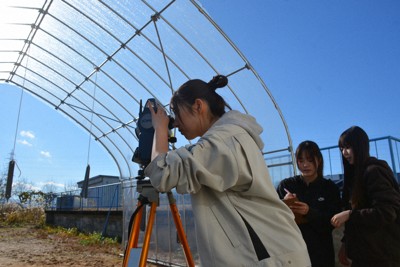 鉄の重りをぶら下げたビニールハウスの特定の点までの距離などを測量機器で測り、値をメモする福井工業高専の学生たち＝福井県鯖江市で2025年12月18日午前11時25分、萱原健一撮影