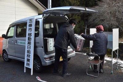 寒空の下、思いを込めた一票を投じる有権者（右）。記載台の奥の地面には、わずかに雪が残る＝五條市西吉野町川股で、山中尚登撮影