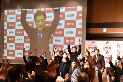 当選が確実となり東京との中継でスクリーンに映し出された木原氏と一緒に万歳する支持者ら＝熊本市中央区で2026年2月8日午後8時4分、山口桂子撮影