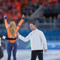 〈届かなかった背中〉スピードスケート女子1000メートルでフィニッシュし、ヨハン・デビット・コーチ（右）から健闘をたたえられる高木美帆（左）。奥は1位となり観客の声援に応えるオランダのユタ・レールダム＝ミラノ・スピードスケート競技場で2026年2月9日、貝塚太一撮影