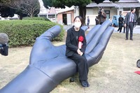 Sadano, the designer of the Evangelion hand sculpture installed in front of JR Ube-Shinkawa Station, is seen sitting on the work in Ube, Yamaguchi Prefecture, on Nov. 20, 2025. (Mainichi/Hiroshi Watanuki)