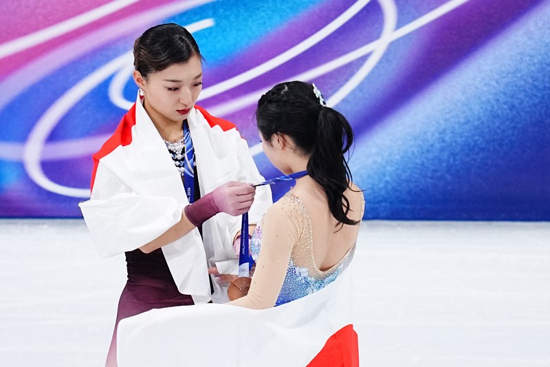 写真撮影を前に中井亜美（手前）のメダルリボンを整える坂本花織＝ミラノ・アイススケートアリーナで2026年2月19日、貝塚太一撮影