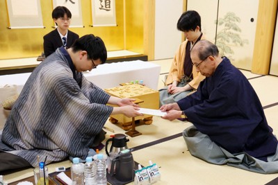 立会の桐山清澄九段（手前右）に封じ手を渡す挑戦者の永瀬拓矢九段（同左）。奥右は藤井聡太王将＝大阪府高槻市の関西将棋会館で2026年3月25日午後6時8分、西村剛撮影