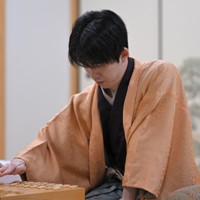 立会の桐山清澄九段（手前右）に封じ手を渡す挑戦者の永瀬拓矢九段（手前左）。奥右は藤井聡太王将＝大阪府高槻市の関西将棋会館で2026年3月25日午後6時8分、西村剛撮影