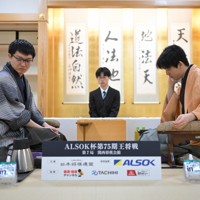 立会の桐山清澄九段（手前右）に封じ手を渡す挑戦者の永瀬拓矢九段（手前左）。奥右は藤井聡太王将＝大阪府高槻市の関西将棋会館で2026年3月25日午後6時8分、西村剛撮影