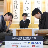 立会の桐山清澄九段（手前右）に封じ手を渡す挑戦者の永瀬拓矢九段（手前左）。奥右は藤井聡太王将＝大阪府高槻市の関西将棋会館で2026年3月25日午後6時8分、西村剛撮影