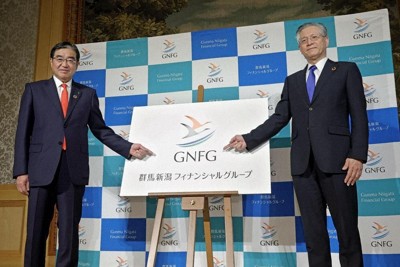 記者会見を終え、新しいロゴマークの前でポーズをとる群馬銀行の深井彰彦頭取（左）と第四北越FGの殖栗道郎社長＝東京都港区で