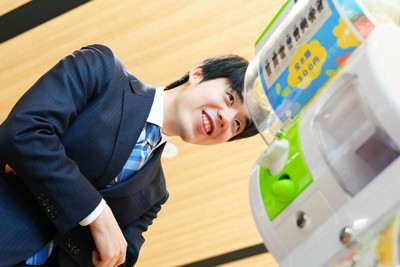 棋士アクリルスタンドのガチャガチャを笑顔でのぞき込む藤井聡太王将＝2026年3月27日（スポーツニッポン新聞社提供）