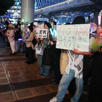 思い思いのプラカードやペンライトを手に静かにスタンディングし、戦争反対の意思表示をする人々＝大阪市北区の阪急うめだ本店前で2026年3月29日午後6時23分、湯谷茂樹撮影