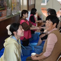 足湯ボランティアで、地域のお年寄りたちと談笑しながら手足をほぐす浜野真衣さん（左）ら大学生たち＝石川県珠洲市野々江町の直公民館で2026年3月28日、中尾卓英撮影