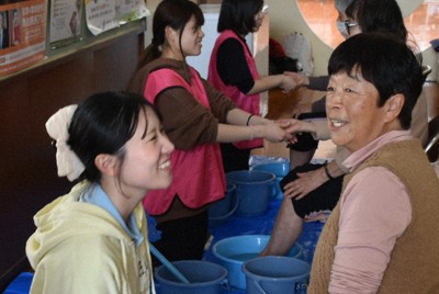 足湯ボランティアで、地域のお年寄りたちと談笑しながら手足をほぐす浜野真衣さん（左）ら大学生たち＝石川県珠洲市野々江町の直公民館で2026年3月28日、中尾卓英撮影