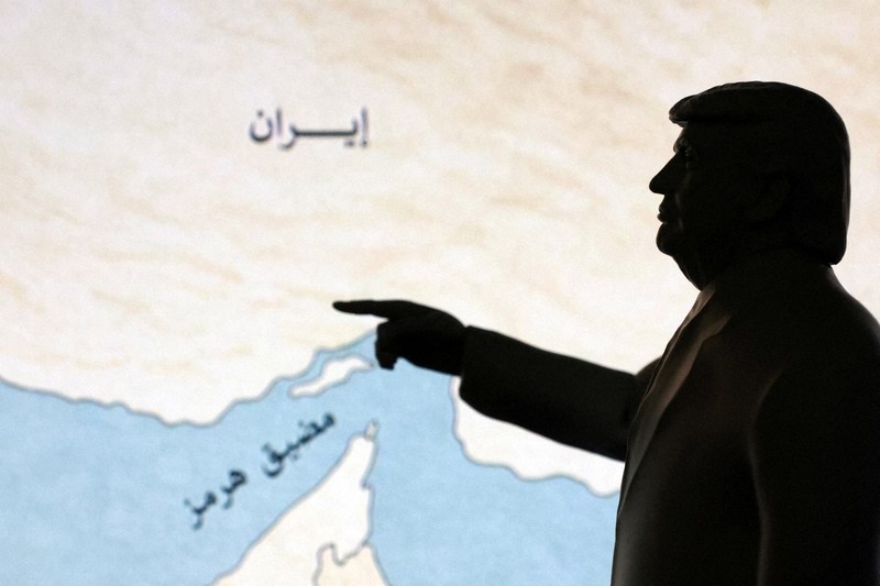 ホルムズ海峡の地図を指さすトランプ米大統領を模したミニチュア＝2026年3月26日、ロイター