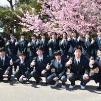 満開の桜の下で、親指で能登半島の形を作って記念撮影をする穴水高校の新入生と教職員ら＝いずれも石川県穴水町で、2026年4月8日午後2時16分、中尾卓英撮影