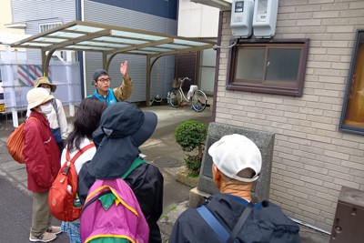 小泉八雲が滞在した家跡の碑に観光客を案内する塚本隆介さん（左手を上げている奥の男性）＝静岡県焼津市で2026年2月23日、小出禎樹撮影