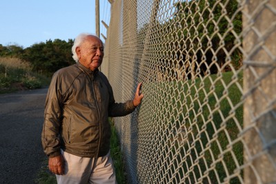 フェンスに囲われた米軍普天間飛行場を見つめる天久英真さん。フェンスのそばにある亀甲墓には姉らの遺骨が納められている＝沖縄県宜野湾市で2026年4月8日午後6時19分、喜屋武真之介撮影