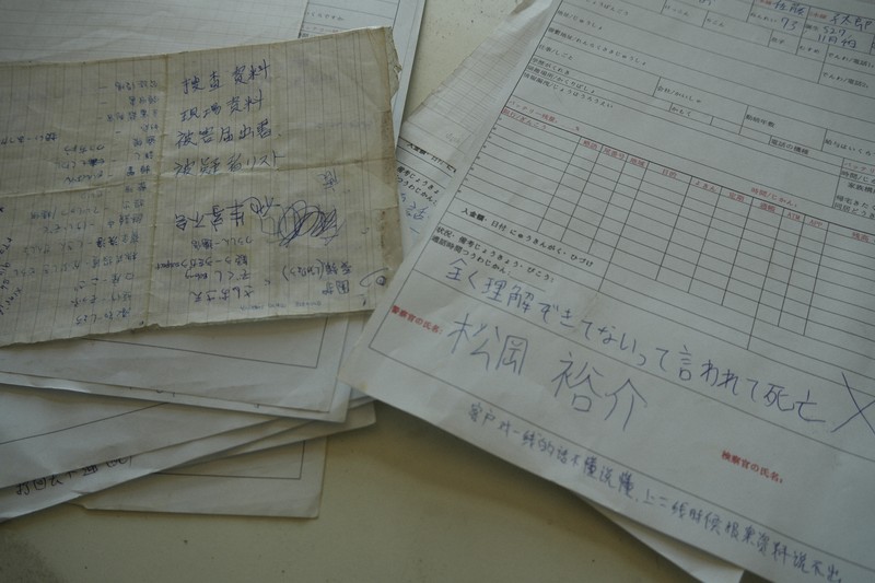 詐欺拠点で見つかった、架電状況などを記した日本語のメモ。警察官役の役名も書かれている＝タイ東北部スリン県近郊のカンボジアとの国境地帯で2026年4月7日、国本愛撮影