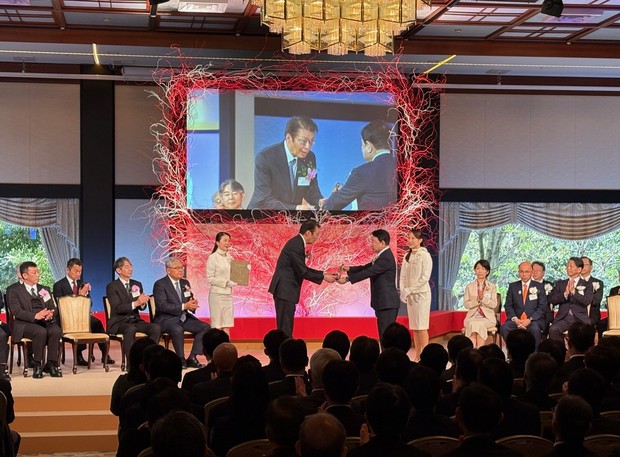 青山繁晴・環境副大臣(中央㊨)から「地球環境大賞」環境大臣賞のトロフィーを授与される増渕智之社長(4月7日、明治記念館=撮影：エコセンター)
