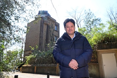 国立天文台(東京都三鷹市)の敷地内に相対性理論の検証のために建てられた通称「アインシュタイン塔」（太陽塔望遠鏡）と本間希樹さん　撮影＝武市公孝