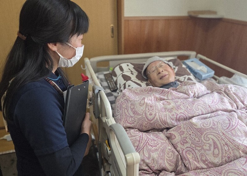 梅田みつよさん（左）の訪問を受け、穏やかな表情を浮かべる男性。末期がんだったが、状態に見合う要介護認定が間に合わないまま、3月初旬に亡くなった＝岐阜県白川町で1月29日、宇多川はるか撮影